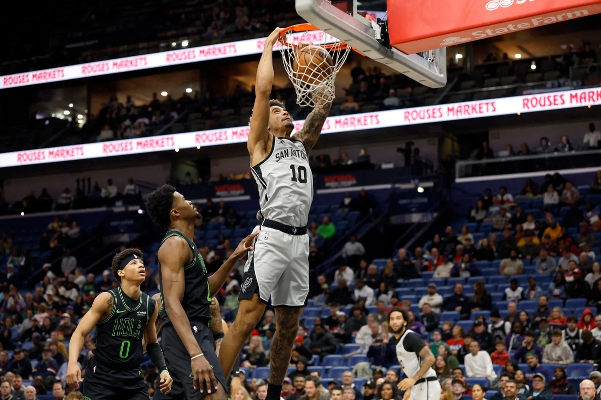 Epizod Jeremiego Sochana w starciu przeciwko New Orleans Pelicans Koszykarz drużyny San Antonio wykorzystuje sytuację pod koszem i wykonuje wsad, w tle widać zawodników drużyny przeciwnej oraz publiczność śledzącą akcję z trybun.