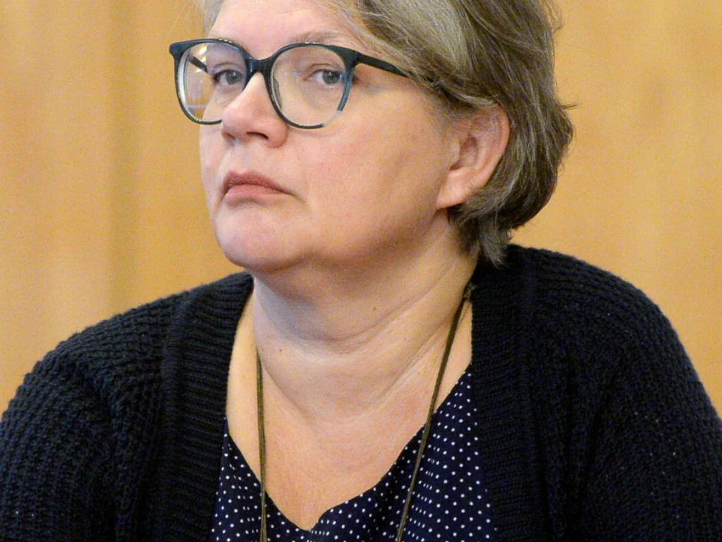 Dorota Zawadzka Kobieta w okularach z krótkimi, siwiejącymi włosami, ubraną w ciemny sweter i granatową bluzkę w kropki, patrząca lekko w bok na neutralnym tle.