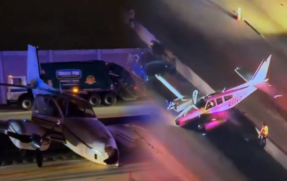 USA. Dwa małe samoloty rozbiły się na amerykańskich drogach w stanie Floryda Dwa małe samoloty znajdują się na drodze przy barierkach betonowych, w pobliżu stoi śmieciarka, a całość jest oświetlona światłami policyjnymi i awaryjnymi. Widać pracownika w kamizelce odblaskowej.