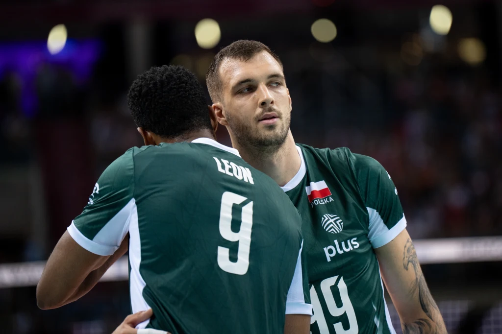 Norbert Huber i Wilfredo Leon Dwóch siatkarzy drużyny narodowej Polski w zielonych koszulkach podczas meczu, jeden z numerem 9 obejmuje drugiego, numer 19, na trykotach widoczne logo sponsora oraz flaga Polski.