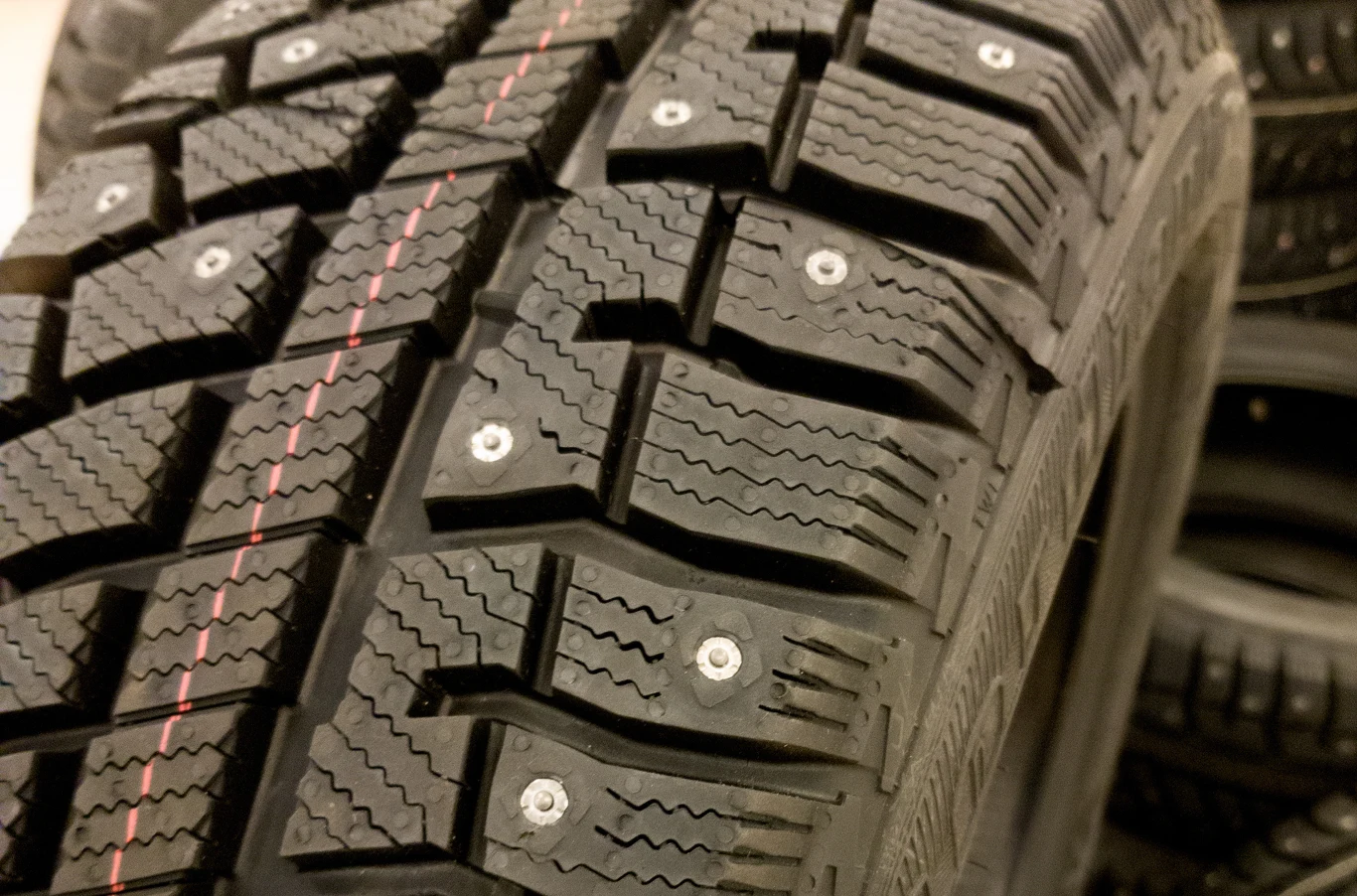 USA rozważają zakaz opon z kolcami. Koszty napraw dróg są ogromne. Bliska perspektywa opony zimowej z wyraźnie widocznymi metalowymi kolcami oraz wyraźnym bieżnikiem, tło rozmyte, widoczne inne opony.