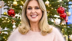 Ewa Wachowicz na tle choinki, ubrana w puchaty sweter w kolorze pudrowego różu