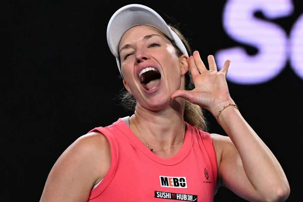 Danielle Collins Tenisistka w sportowym stroju różowego koloru trzyma dłoń przy uchu i szeroko otwiera usta, sugerując gest wołania lub zachęcania kibiców. W tle widoczny ciemny, rozmyty fragment kortu.