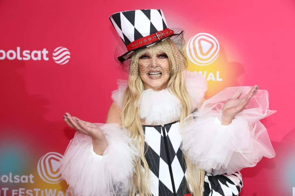 Maryla Rodowicz twierdzi, że cała jej emerytura nie wystarczy nawet na wykarmienie jej kotów Kobieta w efektownym stroju arlekina z charakterystycznymi biało-czarnymi rombami i wysokim kapeluszem z woalką pozuje na tle różowej ścianki z logotypami festiwalu.