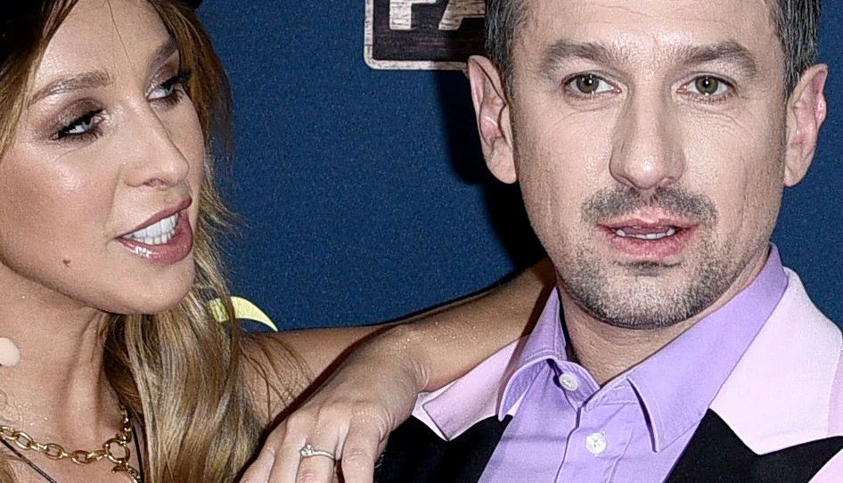 Ilona Krawczyńska, Maciej Rock Para ubrana elegancko, kobieta z blond włosami obejmuje mężczyznę w koszuli z jasnym kołnierzykiem, w tle ciemnoniebieska ścianka zdjęciowa z widocznymi fragmentami logotypów.