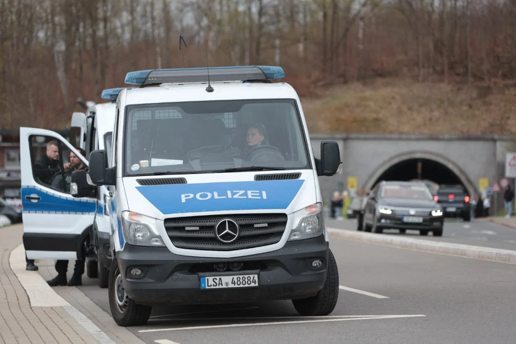 Polak spowodował wypadek na niemieckiej autostradzie. Policja przeprowadziła pościg za 41-latkiem. Zdj. ilustracyjne Radiowóz niemieckiej policji stoi zaparkowany przy drodze, drzwi od strony kierowcy są otwarte, w pobliżu znajduje się funkcjonariusz, w tle widoczny tunel, kilka samochodów oraz krajobraz z drzewami bez liści.
