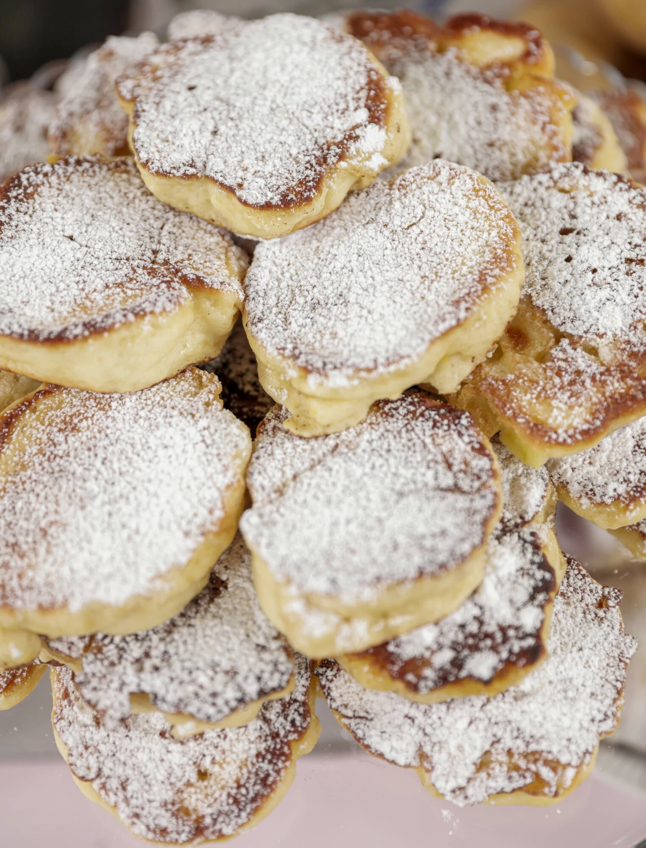 Stos puszystych placuszków posypanych obficie cukrem pudrem, rumiane brzegi, deser ułożony warstwami na talerzu.