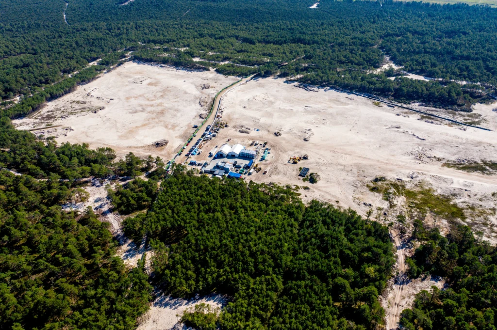 Komisja Europejska zatwierdziła wniosek Polski o udzielenie pomocy publicznej na budowę elektrowni jądrowej Rozległy, piaszczysty teren otoczony gęstym lasem, w centralnej części znajdują się namioty i zabudowania stanowiące tymczasową infrastrukturę budowlaną oraz pojazdy rozmieszczone w okolicy.