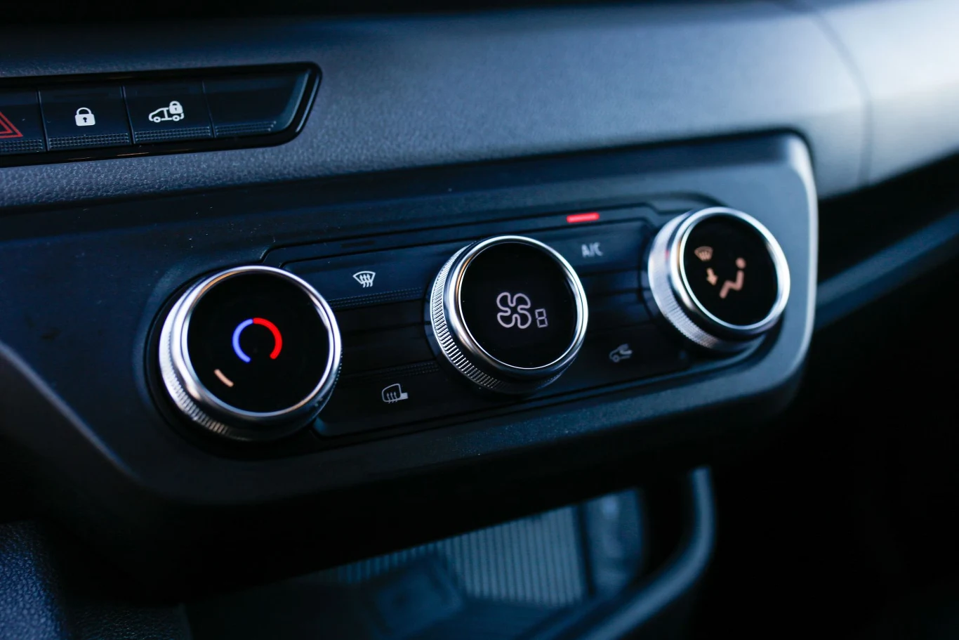 Panel klimatyzacji samochodowej z trzema pokrętłami do regulacji temperatury, siły nadmuchu oraz rozprowadzania powietrza, z widocznymi ikonami i podświetleniem.