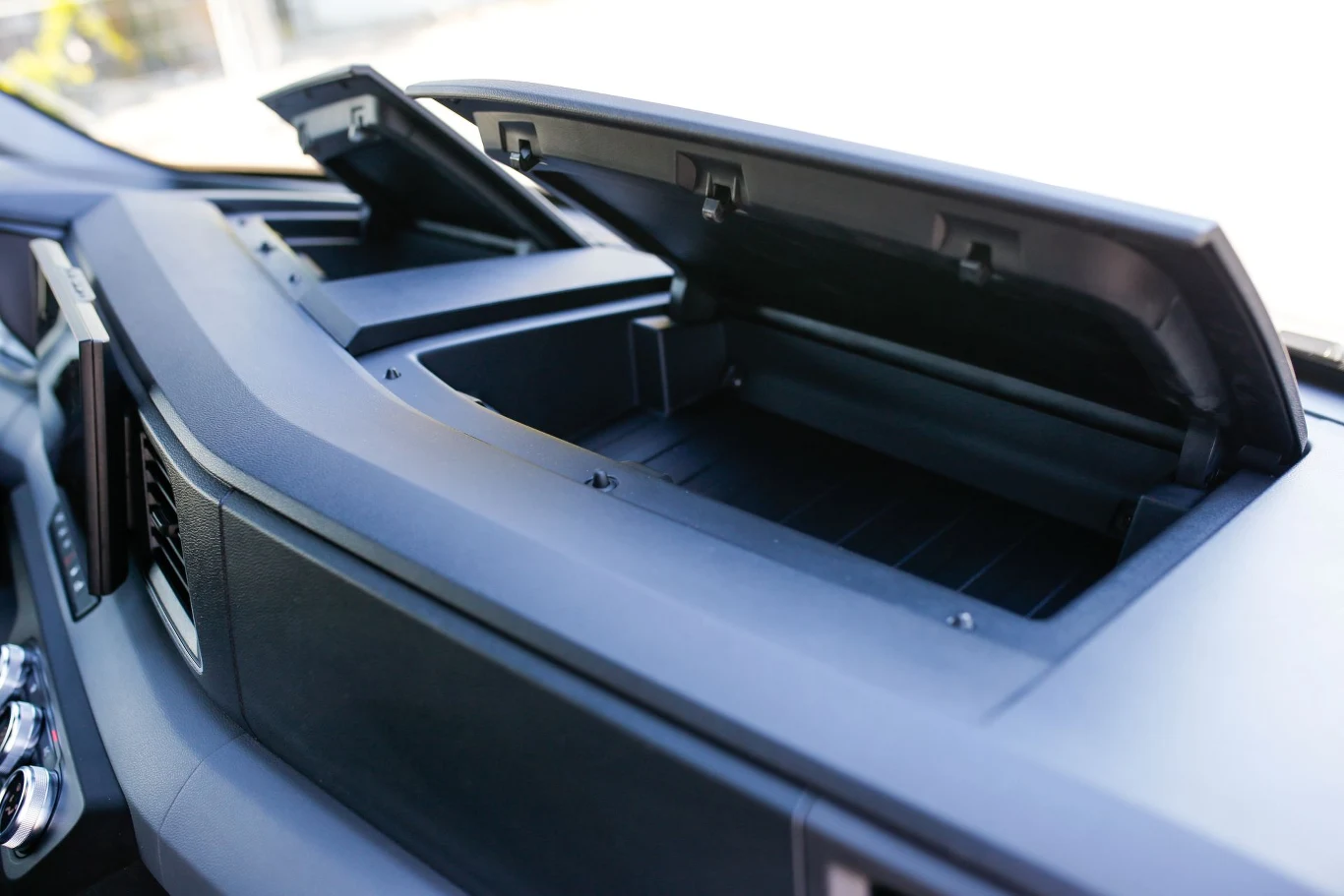 Otwarty schowek w desce rozdzielczej samochodu z widocznym podłużnym wnętrzem, plastikową obudową oraz czarnym wykończeniem wokół przestrzeni na drobiazgi.