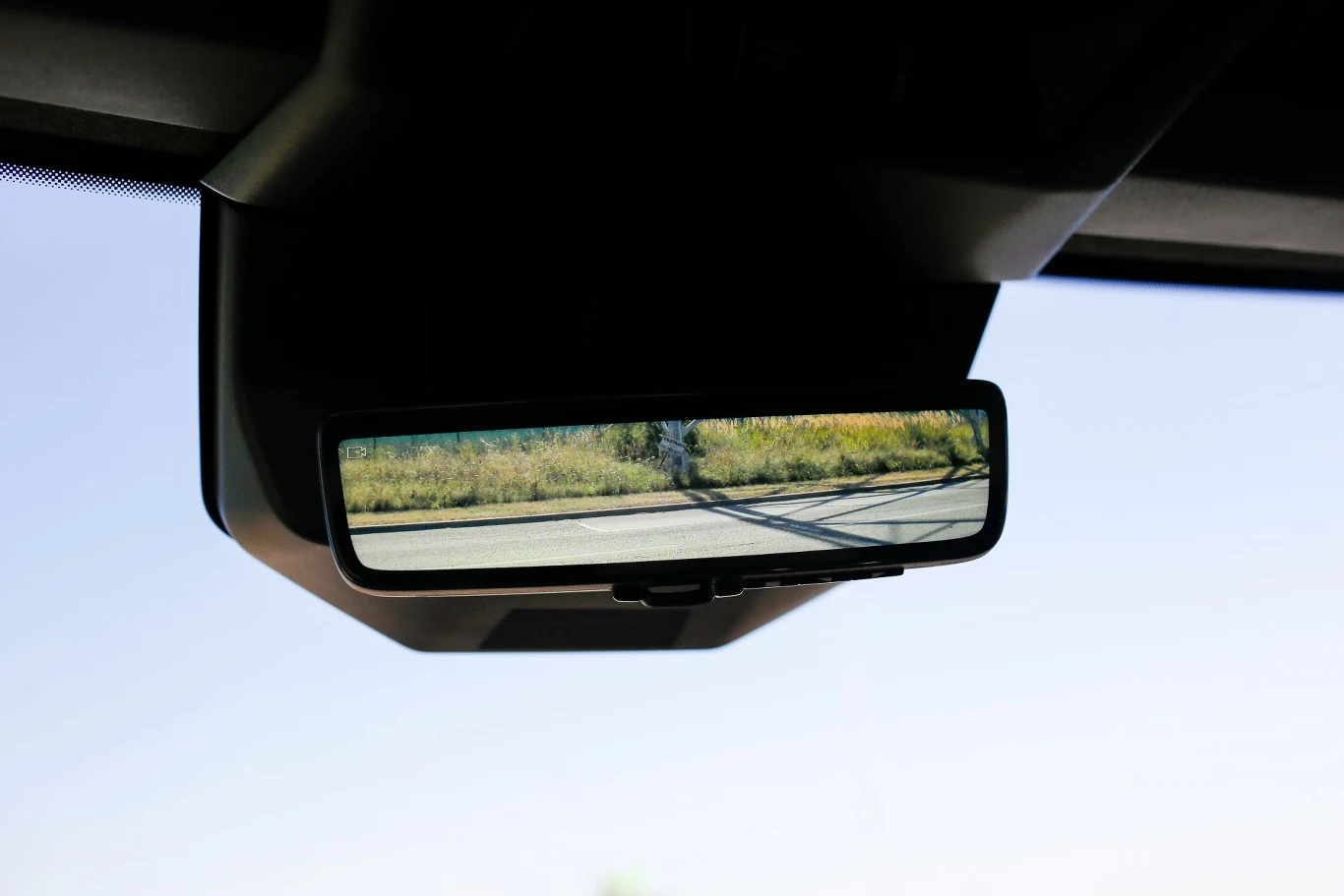 Widok w lusterku wstecznym samochodu, odbijający fragment zieleni przy drodze oraz kawałek ulicy, z wnętrzem pojazdu w tle.