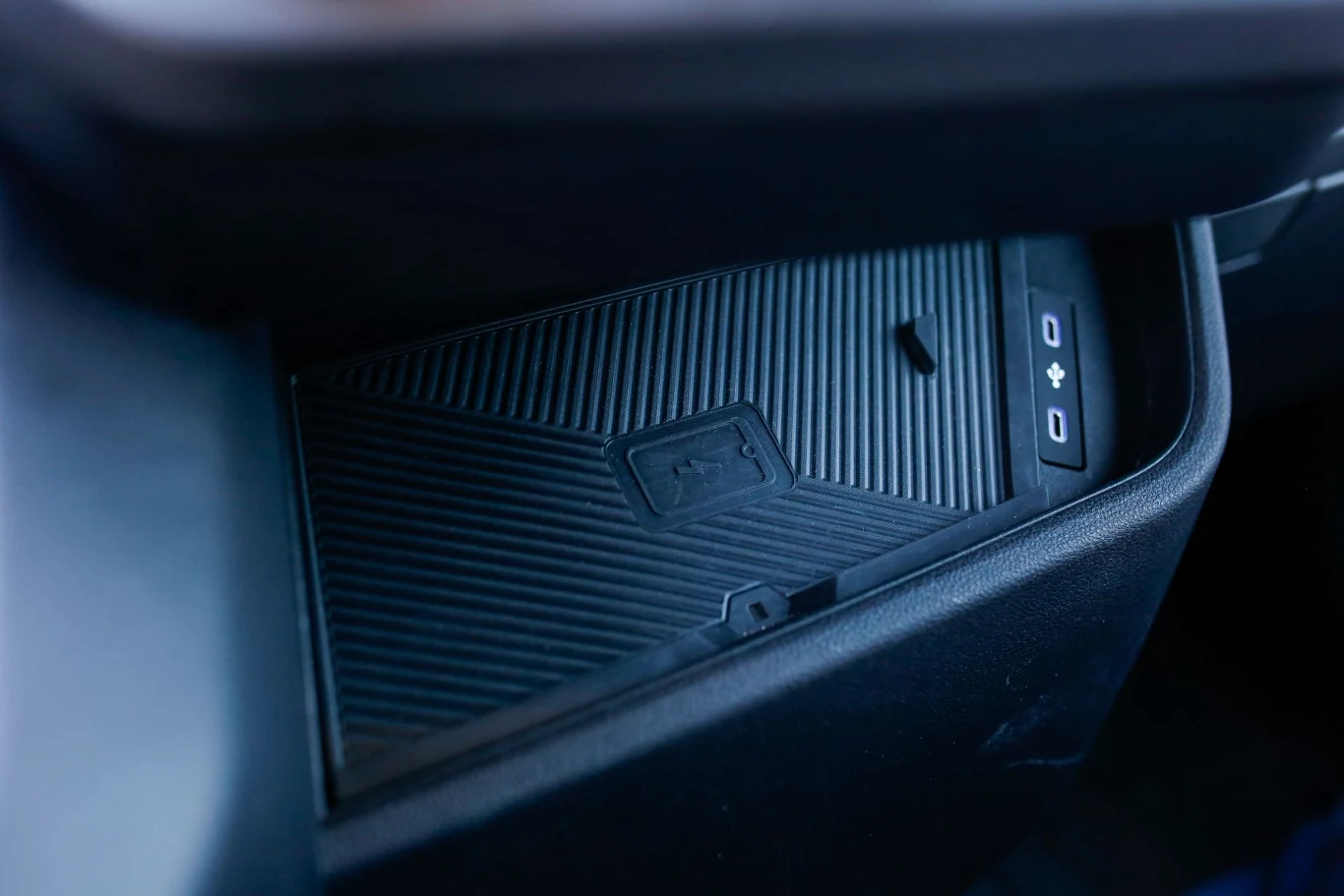 Powierzchnia ładowarki indukcyjnej w samochodzie z widocznymi przyciskami sterowania i strukturą antypoślizgową.