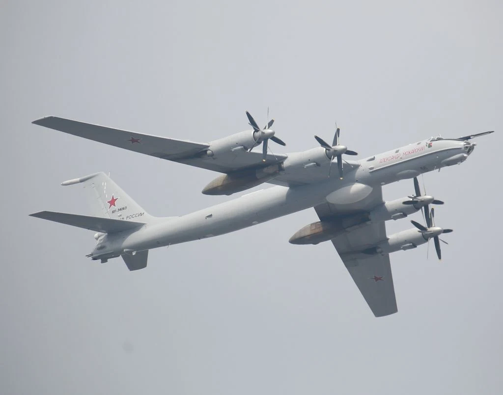 Rosyjski bombowiec Tu-95 (zdj. ilustracyjne) Wojskowy samolot bombowy o charakterystycznym układzie czterech silników turbośmigłowych, srebrnoszare malowanie z czerwonymi gwiazdami na skrzydłach i ogonie, lecący na tle jednolitego nieba.