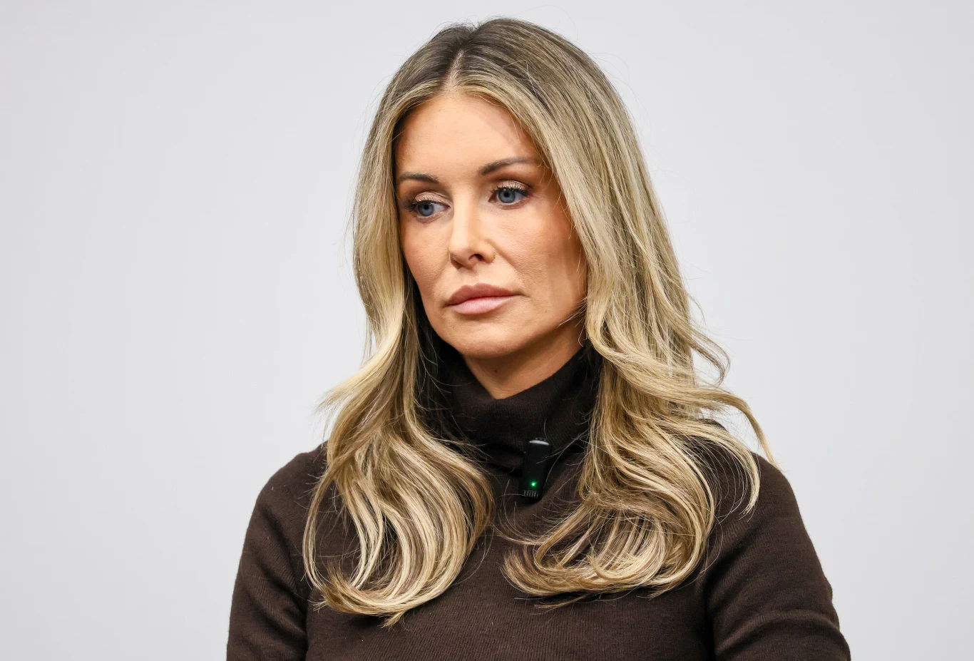 Małgorzata Rozenek-Majdan Kobieta o długich blond włosach i jasnych oczach, ubrana w ciemny golf, patrząca poważnie w bok na jasnoszarym tle.