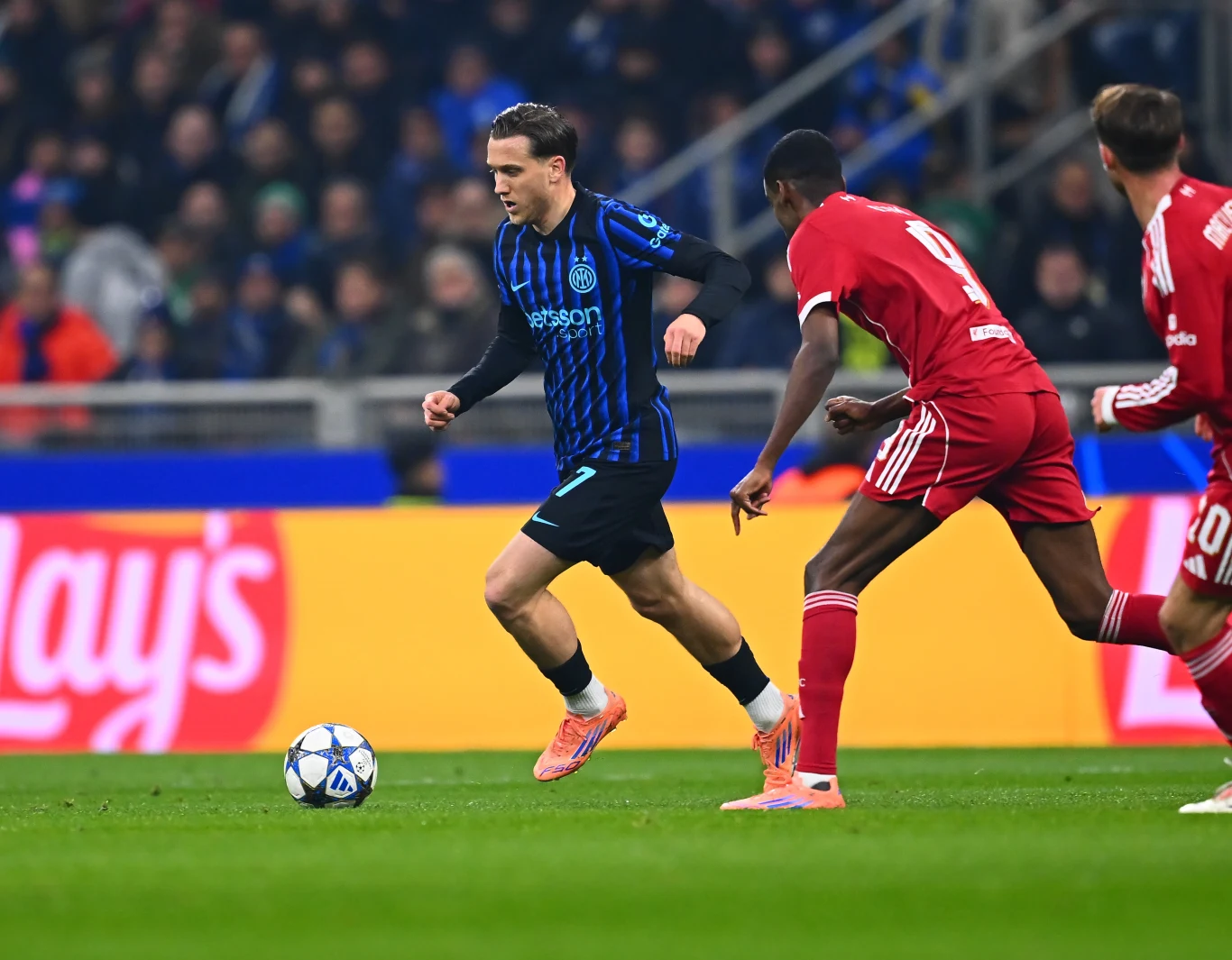 Piotr Zieliński podczas meczu z Liverpoolem Piłkarz w niebiesko-czarnym stroju prowadzi piłkę, podczas gdy dwóch zawodników w czerwonych strojach próbuje go powstrzymać na stadionie w trakcie meczu piłki nożnej.