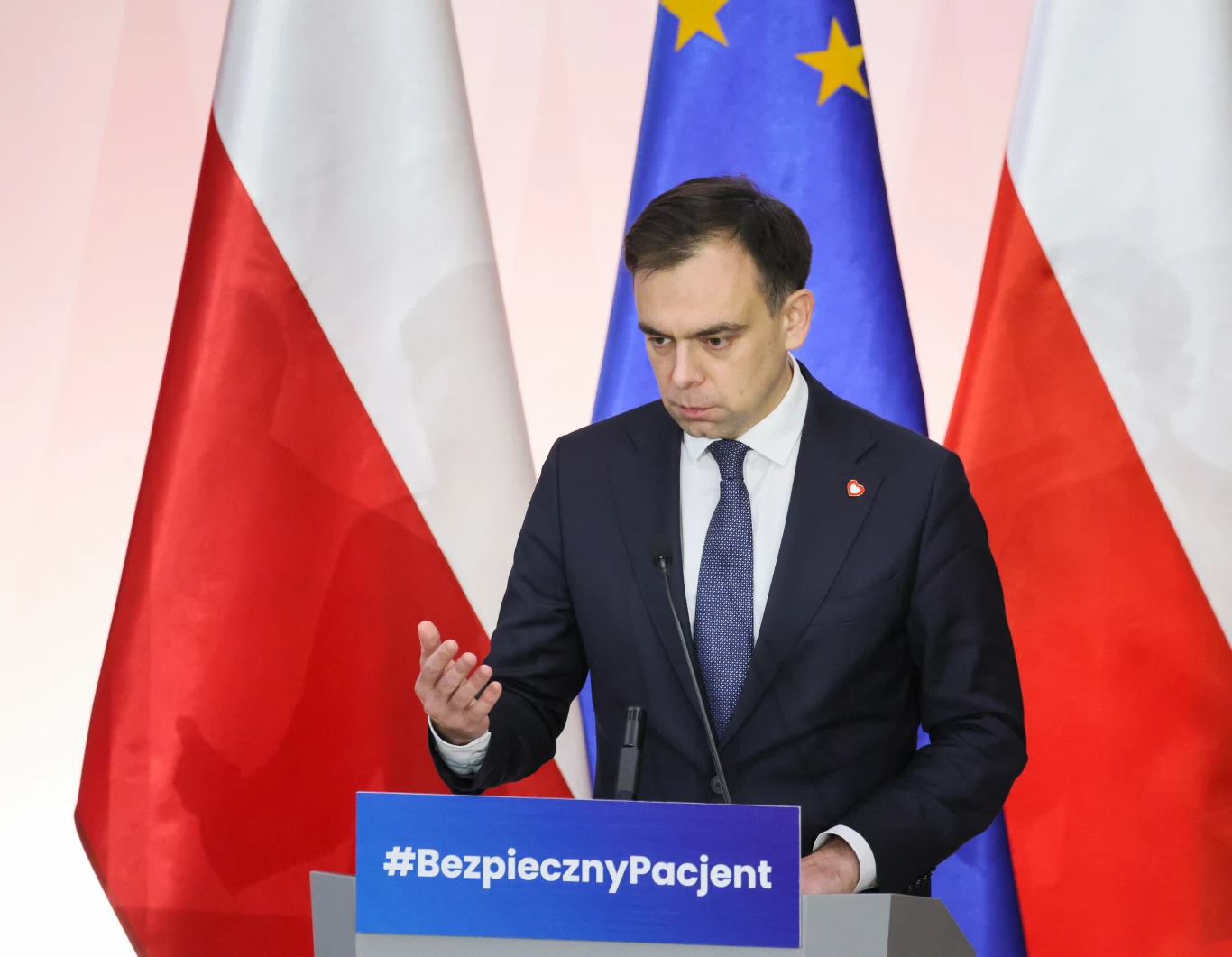 Minister finansów Andrzej Domański uważa, że w obecnych warunkach nie można na nowo otwierać dyskusji o obniżeniu składki zdrowotnej Mężczyzna w garniturze przemawia przy mównicy z napisem #BezpiecznyPacjent, w tle widoczne są flagi Polski i Unii Europejskiej.