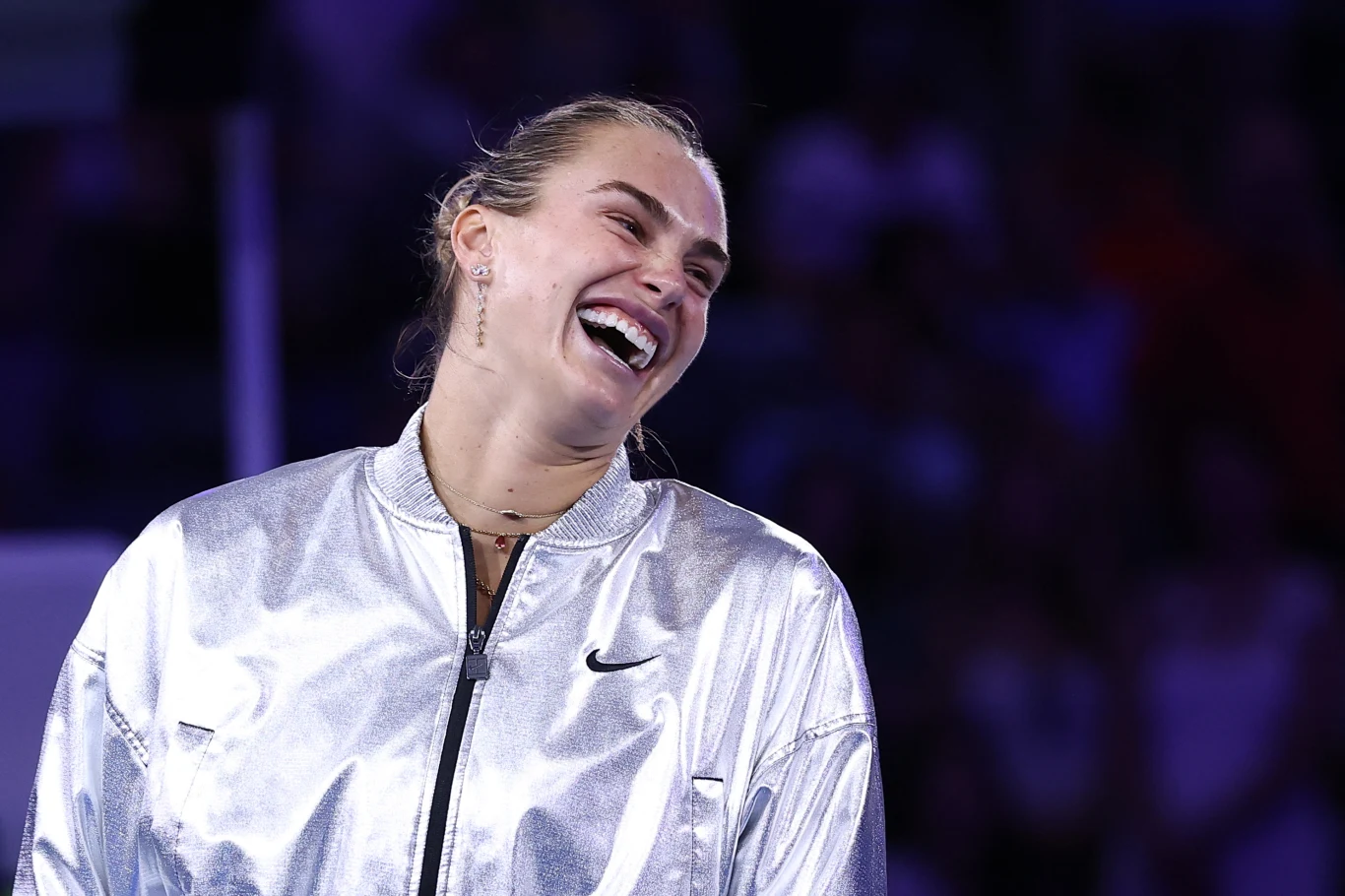 Aryna Sabalenka zdradziła, czy zamierza zmienić narodowość Uśmiechnięta młoda kobieta w srebrnej, sportowej kurtce stoi na tle rozmazanego tłumu, wyrażając radość i pozytywną energię.