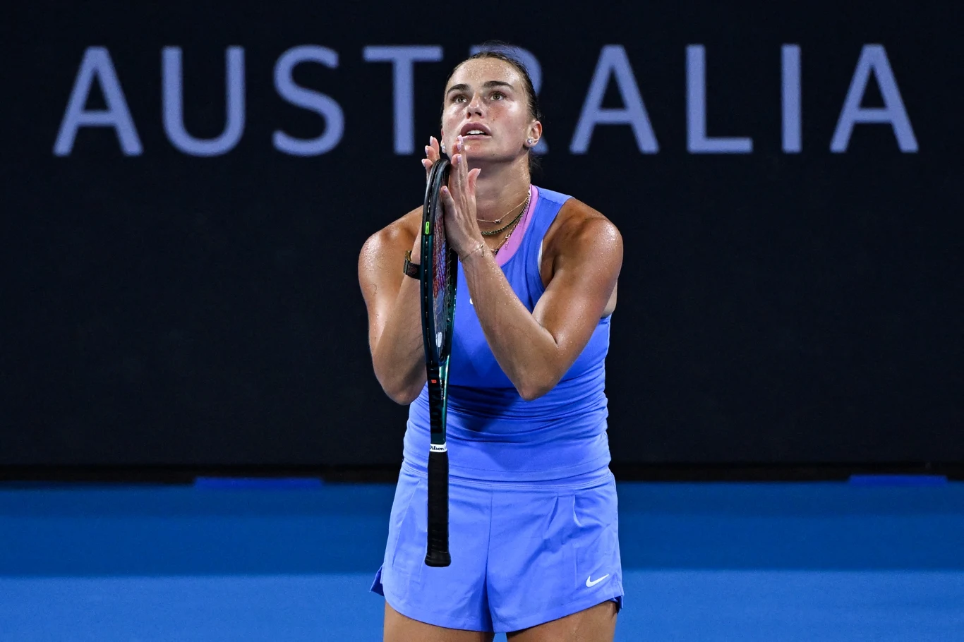 Aryna Sabalenka, Brisbane 2025 Tenisistka w niebieskim stroju sportowym, z rakietą w rękach skierowanych ku górze, stojąca na korcie na tle napisu AUSTRALIA. Jej wyraz twarzy sugeruje silne emocje, prawdopodobnie podsumowanie ważnego momentu meczu.