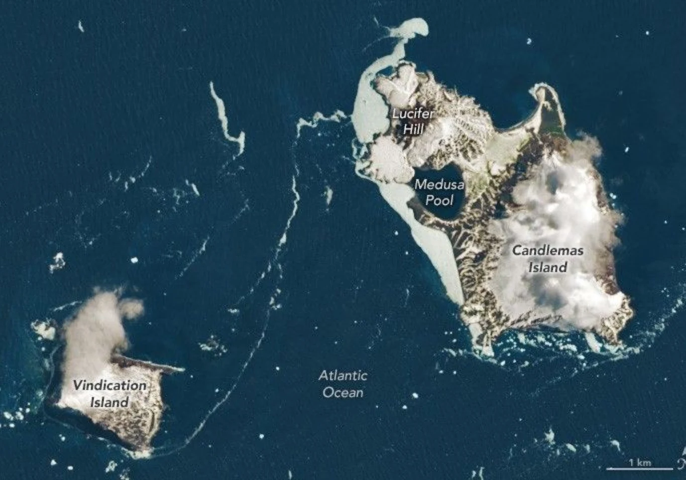 Widok satelitarny dwóch wysp położonych na Oceanie Atlantyckim. Na mapie oznaczone są nazwy geograficzne, takie jak Vindication Island, Candlemas Island, Lucifer Hill oraz Medusa Pool. Wyspy otoczone są wodą, widoczne są także chmury unoszące się nad l...