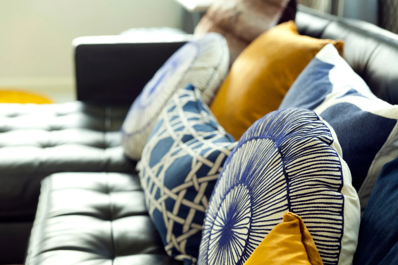 Czarne skórzane siedzisko ozdobione kolorowymi poduszkami w geometryczne wzory oraz w odcieniach niebieskiego i musztardowego.