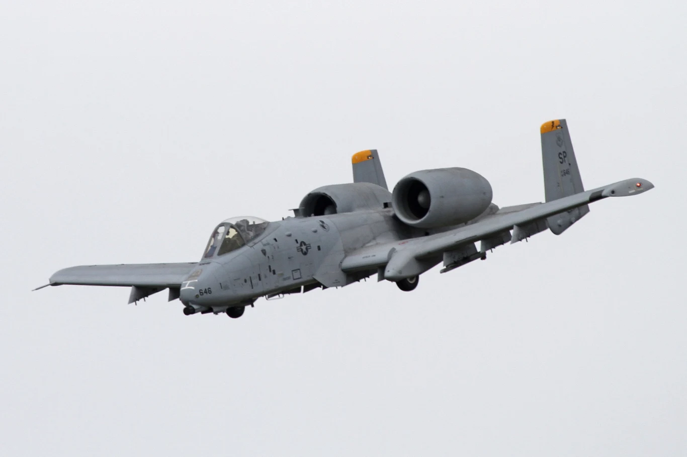 A-10 Thunderbolt II nazywany jest często "działem ze skrzydłami" Samolot szturmowy A-10 Thunderbolt II w locie na tle pochmurnego nieba, charakterystyczny podwójny silnik i skrzydła z uzbrojeniem widoczne z boku.