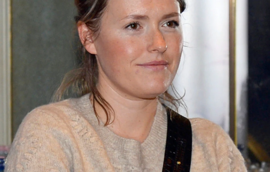 Młoda kobieta z lekko upiętymi włosami, ubrana w beżowy sweter, siedzi zwrócona w stronę aparatu z neutralnym wyrazem twarzy.