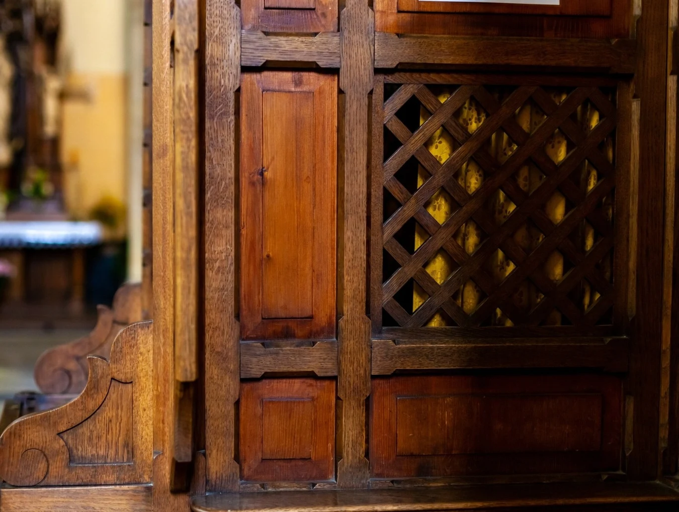 Spowiedź przed świętami Bożego Narodzenia. Czy jest obowiązkowa? Drewniana konfesjonał z bogato zdobioną kratką, widoczne są szczegóły konstrukcji i rzeźbienia drewna, w tle lekko rozmyte elementy wnętrza kościoła.