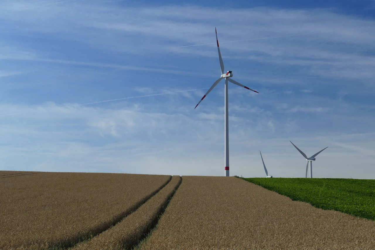 Farma wiatrowa Nowoczesne wiatraki stojące na polu uprawnym, niebo pokryte delikatnymi chmurami, w tle kolejne turbiny wiatrowe – krajobraz sprzyjający odnawialnym źródłom energii.