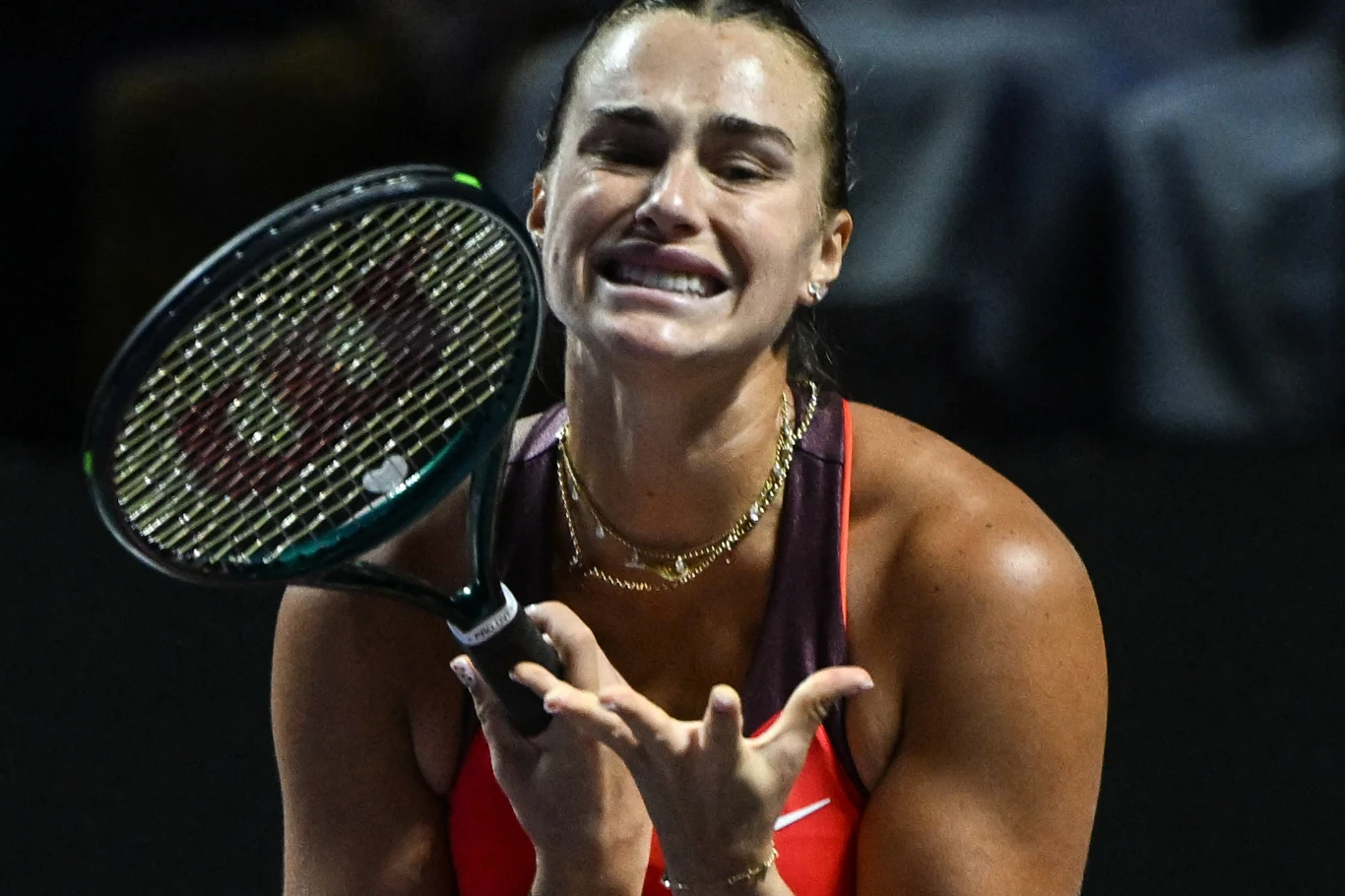 Zawodniczka tenisowa w dynamicznej pozie z wyraźnie widocznymi emocjami, trzymająca rakietę tenisową i ubrana w sportowy strój, na tle zamazanego stadionu.