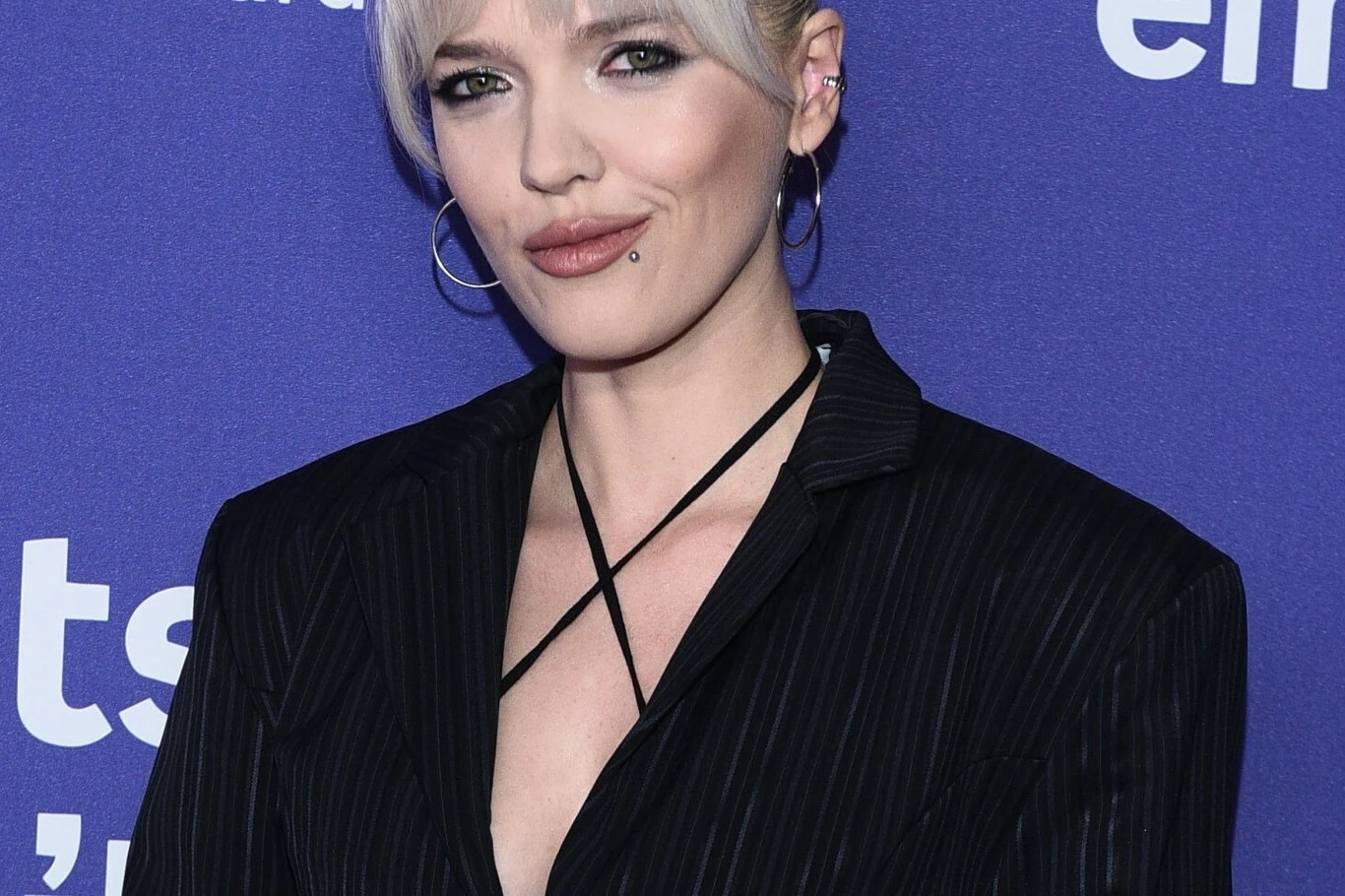 Daria Zawiałow ogłasza powrót do koncertowania Kobieta z krótkimi, jasnymi włosami, w dużych kolczykach i eleganckim czarnym żakiecie, na fioletowym tle z białymi napisami.