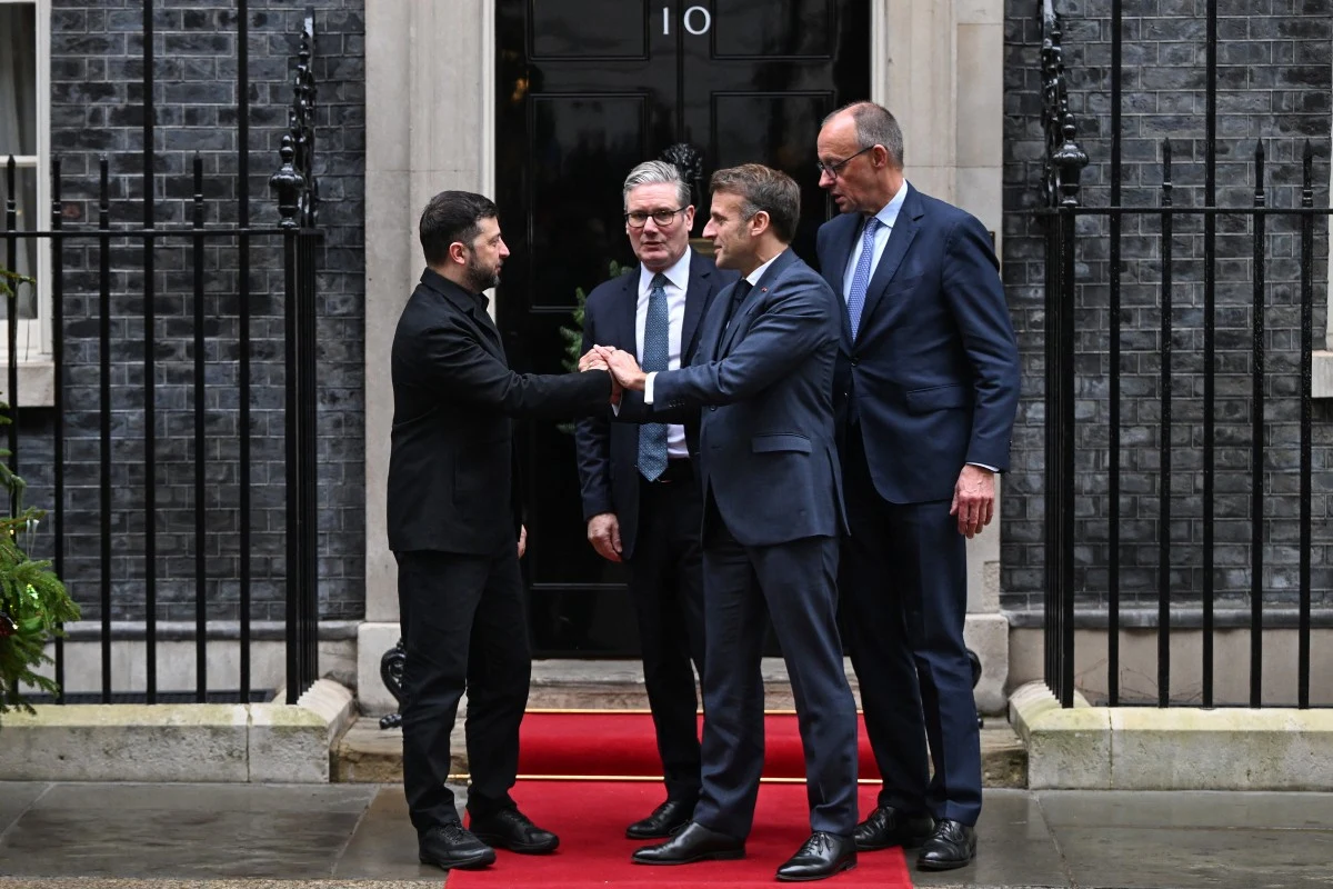 Spotkanie Wołodymyra Zełenskiego z Keirem Starmerem, Emmanuelem Macronem i Friedrichem Merzem w Londynie Czterech mężczyzn w formalnych garniturach stoi na czerwonym dywanie przed wejściem do budynku oznaczonego numerem 10, dwóch z nich ściska sobie dłonie, atmosfera jest oficjalna i poważna.