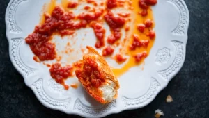 biały talerz z resztkami sosu pomidorowego i kawałkiem chleba do "wylizania" talerza