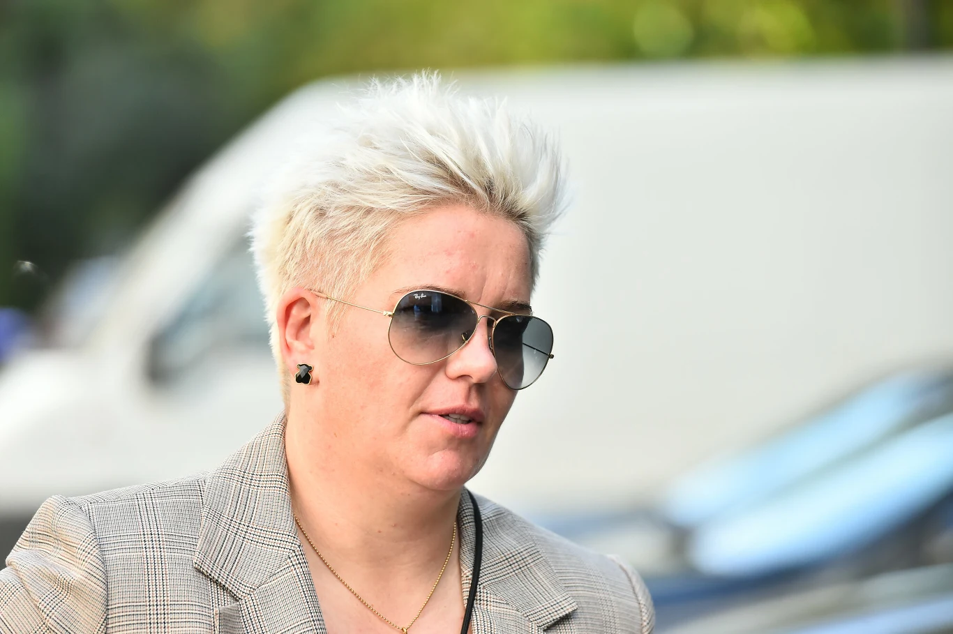 Anita Włodarczyk Osoba z krótkimi, jasnymi włosami nosząca okulary przeciwsłoneczne oraz elegancką marynarkę, widoczna na tle rozmytego miejskiego otoczenia.