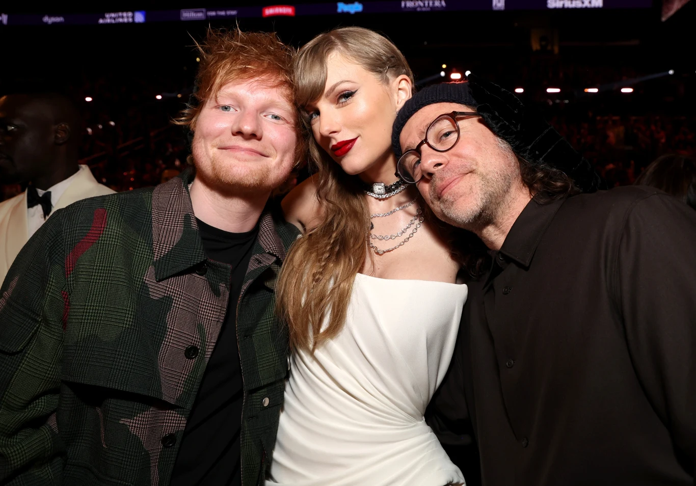 Ed Sheeran i Taylor Swift z Aaronem Dessnerem podczas rozdania nagród Grammy Trzy osoby pozujące razem na tle sali koncertowej, kobieta w białej sukni pośrodku, dwaj mężczyźni po obu stronach, wszyscy uśmiechnięci i skierowani w stronę obiektywu.