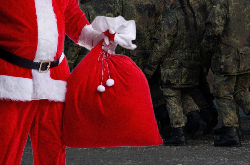 Święci mikołajowie z Bundeswehry. Przechadzali się po jarmarku z bronią Postać w stroju świętego Mikołaja trzymająca duży czerwony worek, w tle widoczni żołnierze w mundurach ustawieni w szeregu.