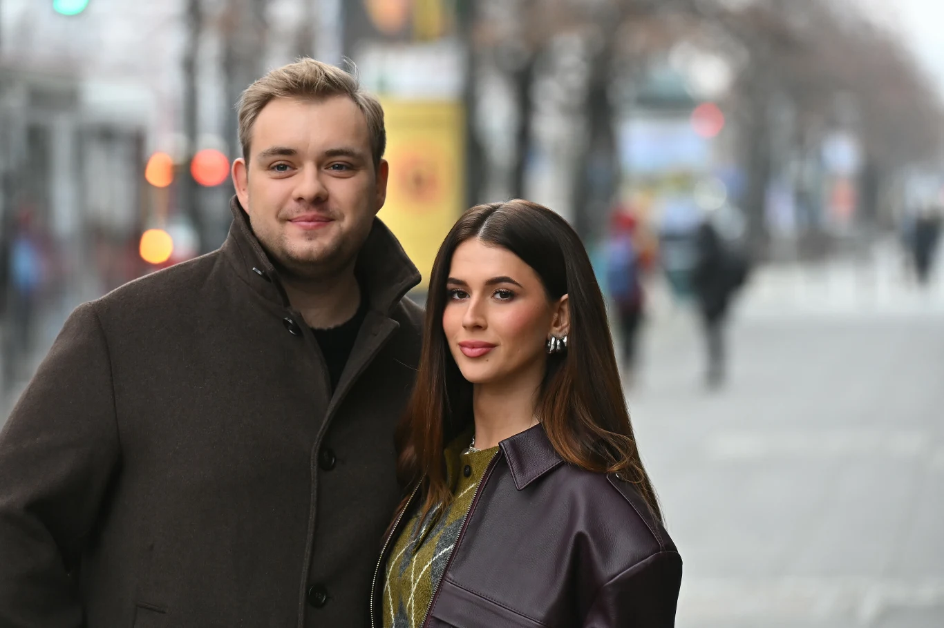 Roxie Węgiel w 2024 r. poślubiła Kevina Mgleja Młody mężczyzna i kobieta stoją razem na tle miejskiej ulicy, ubrani w modne, zimowe płaszcze, patrzą prosto w obiektyw z delikatnym uśmiechem. W tle widoczne rozmazane światła miasta oraz przechodnie.