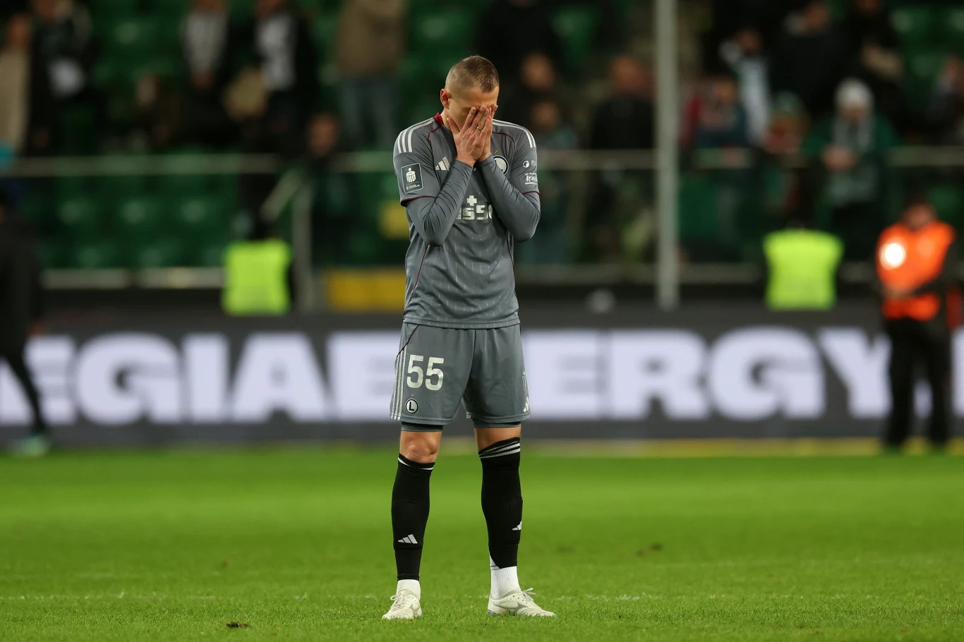 Legia przegrała nawet z Bruk-Betem Termaliką Nieciecza Piłkarz w szarej koszulce zakrywający twarz dłońmi, stojący na murawie stadionu, w tle niewyraźni kibice i ochrona.