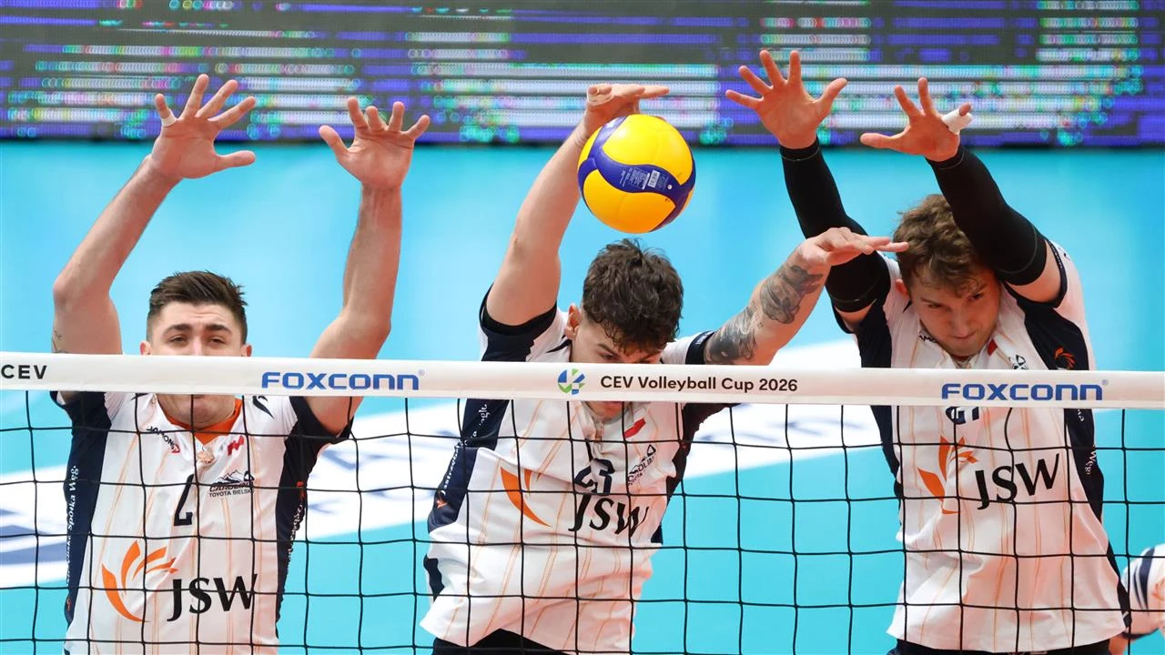 Trzech siatkarzy próbujących zablokować piłkę nad siatką podczas meczu siatkówki, dynamiczna akcja przy siatce, widoczne koszulki zespołu JSW i napis CEV Volleyball Cup 2026 na bandzie reklamowej.