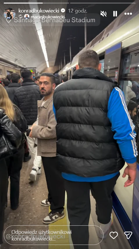 Konrad Bukowiecki na stacji Santiago Bernabeu Tłum ludzi oczekujący na peronie metra obok otwartych drzwi pociągu, w centrum kadru mężczyzna patrzący w stronę obiektywu, większość osób stoi tyłem lub bokiem, pod sufitem charakterystyczne oświetlenie peronu.