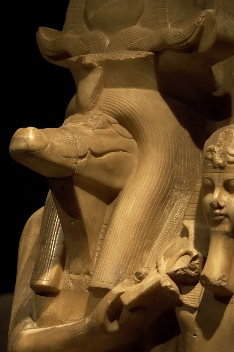 Sobek to egipski bóg przedstawiany z głową krokodyla Starożytna rzeźba z Egiptu przedstawiająca postać z głową krokodyla, prawdopodobnie wizerunek Sobka, egipskiego boga wody, z widocznym fragmentem innej postaci po prawej stronie.