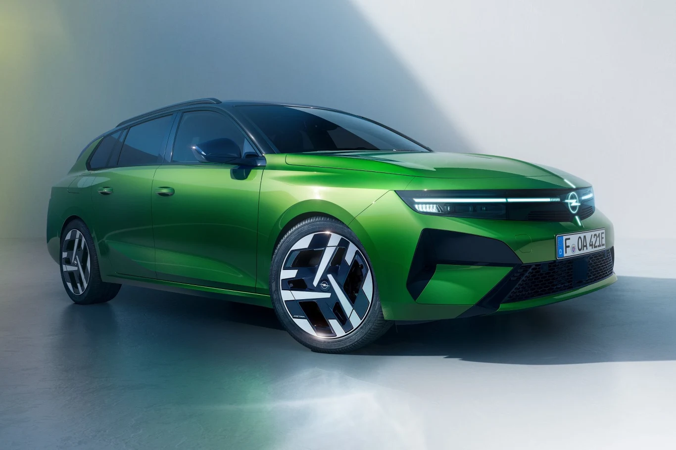 Opel Astra doczekał się modernizacji. Co się zmieniło? Nowoczesny zielony samochód osobowy typu kombi z charakterystycznymi, agresywnie zarysowanymi reflektorami LED, dużymi, designerskimi felgami oraz opływową sylwetką, ustawiony w jasnym, minimalistycznym otoczeniu.