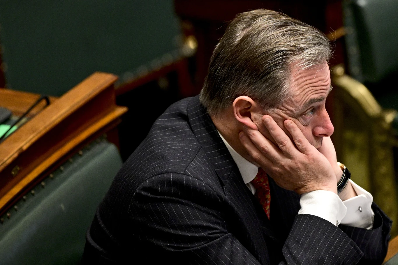 Belgijski premier Bart de Wever staje w obliczu presji ze strony UE w związku z wykorzystaniem zamrożonych rosyjskich aktywów Mężczyzna w garniturze siedzi z dłońmi opartymi o twarz, wyraża zamyślenie lub zmartwienie, tło stanowi wnętrze sali obrad z widocznymi ławkami i stołem.