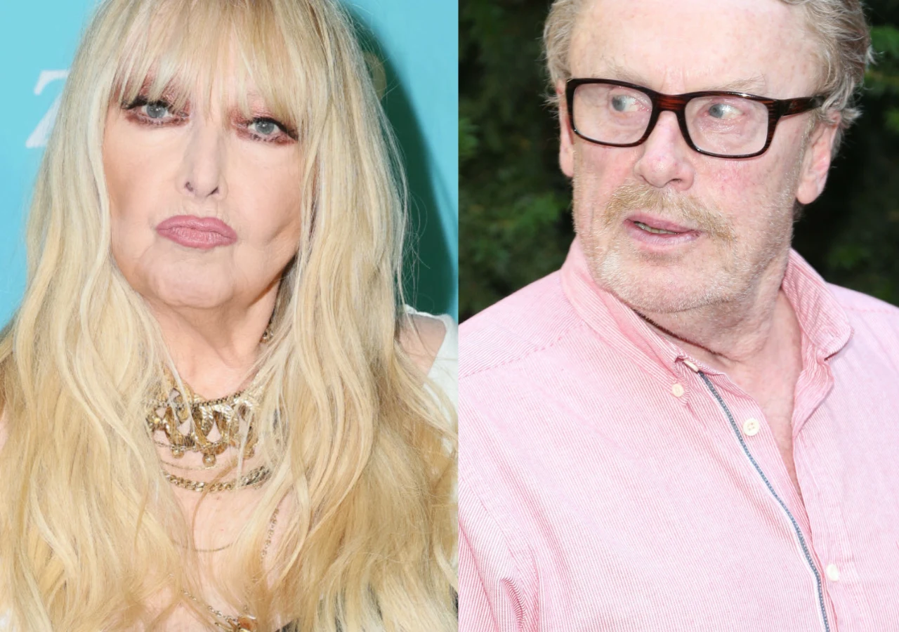 Dwie osoby na zdjęciu, kobieta z długimi blond włosami, makijażem i obfitą biżuterią po lewej stronie oraz mężczyzna w okularach, w różowej koszuli, spoglądający w bok po prawej stronie.