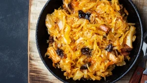 Bigos w garnku, widok z góry. Stoi na stole, w bigosie widoczne dodatki - mięso i suszone śliwki