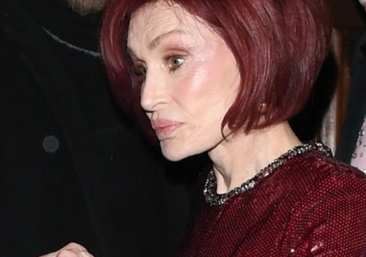 Sharon Osbourne Kobieta o krótkich, ciemnoczerwonych włosach w eleganckiej, czerwonej sukni z błyszczącymi detalami, patrząca w bok. Wyeksponowany makijaż dodaje wyrazistości rysom twarzy.