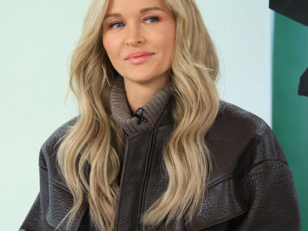 Joanna Krupa Młoda kobieta o długich blond włosach ubrana w ciepły golf i ciemną, skórzaną kurtkę, patrzy lekko uśmiechnięta w bok, na jasnym tle.