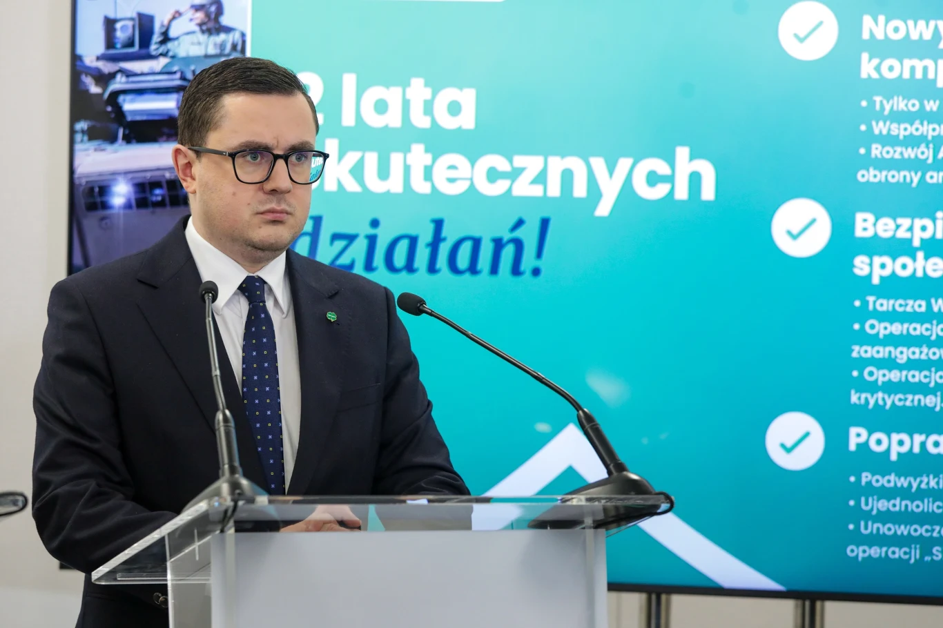 Polska może stać się północną bramą gazową do Europy - mówił minister energii Miłosz Motyka podczas uroczystości 10-lecia Terminala LNG w Świnoujściu Mężczyzna w garniturze i okularach stoi za mównicą podczas konferencji prasowej, w tle widoczny jest ekran z hasłem '2 lata skutecznych działań' oraz wypunktowanymi informacjami.