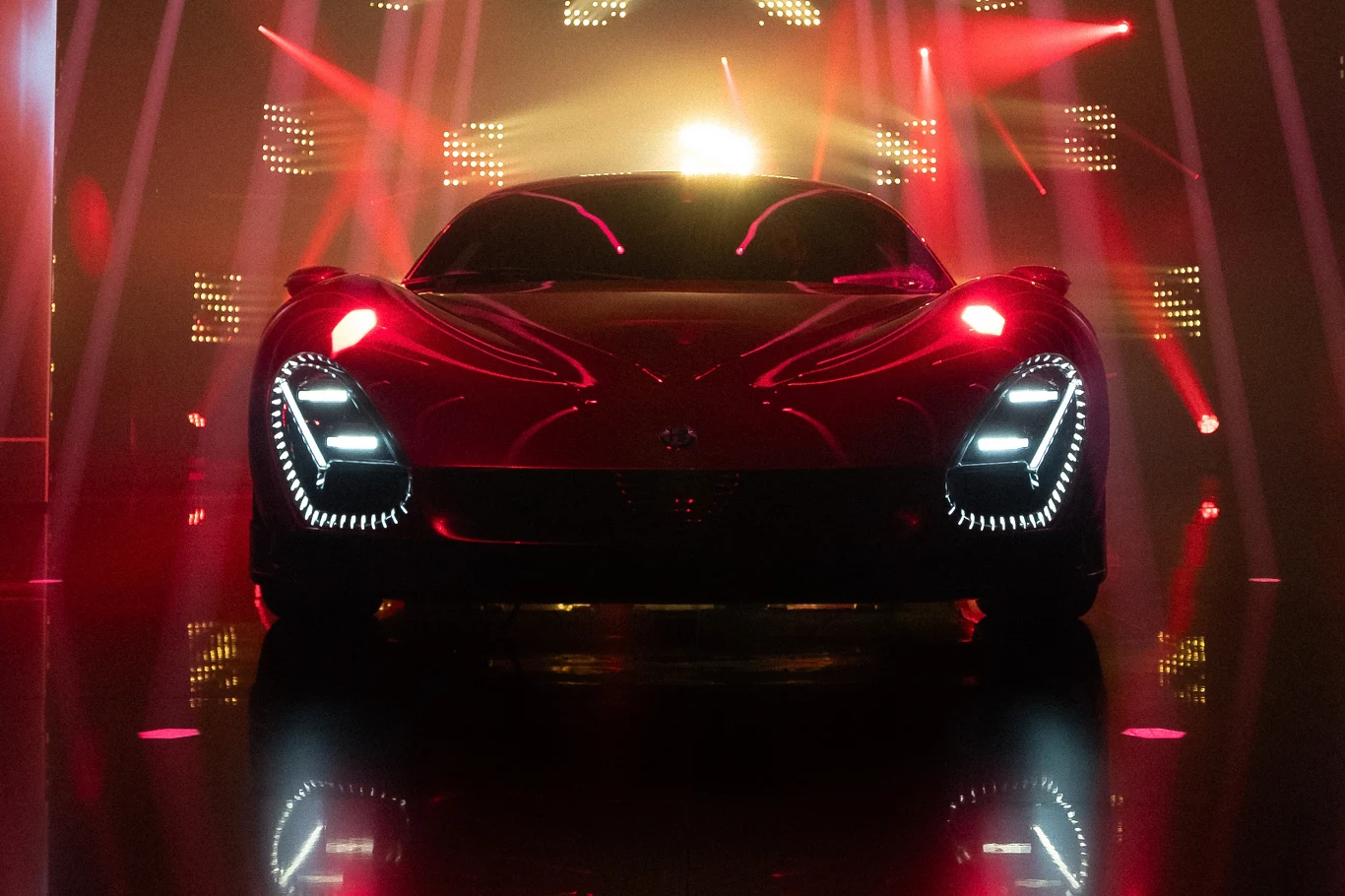 Alfa Romeo i Maserati będą pracować nad wyjątkowymi samochodami dla najbogatszych klientów Nowoczesny czerwony supersamochód sportowy o dynamicznej sylwetce stoi na podświetlonej scenie z intensywnym, kolorowym oświetleniem LED oraz światłami reflektorów skierowanymi na pojazd, co podkreśla jego agresywny wygląd i futurystyczne detale.