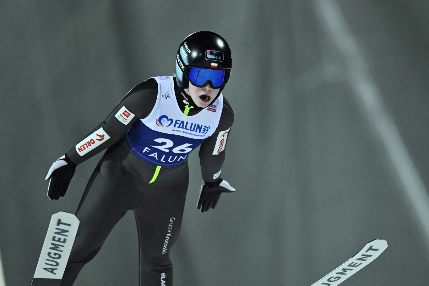 Wisła ma "stracić" zawody Pucharu Świata Skoczek narciarski w kombinezonie i kasku podczas lotu w trakcie zawodów na tle nocnej skoczni, widoczny numer startowy i oznaczenia sponsora, tło rozmyte.