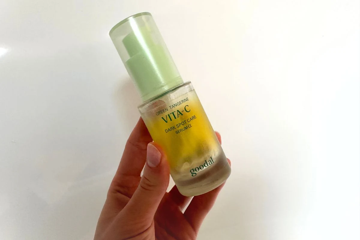 Ręka trzyma szklaną butelkę z serum do twarzy marki Goodal z serii Vita C, posiadającej żółty płyn i zieloną nakrętkę.